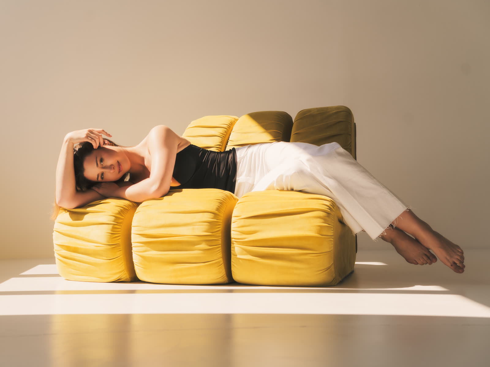 Women's session in a Kraków studio — model resting on a yellow sofa in a band of natural light