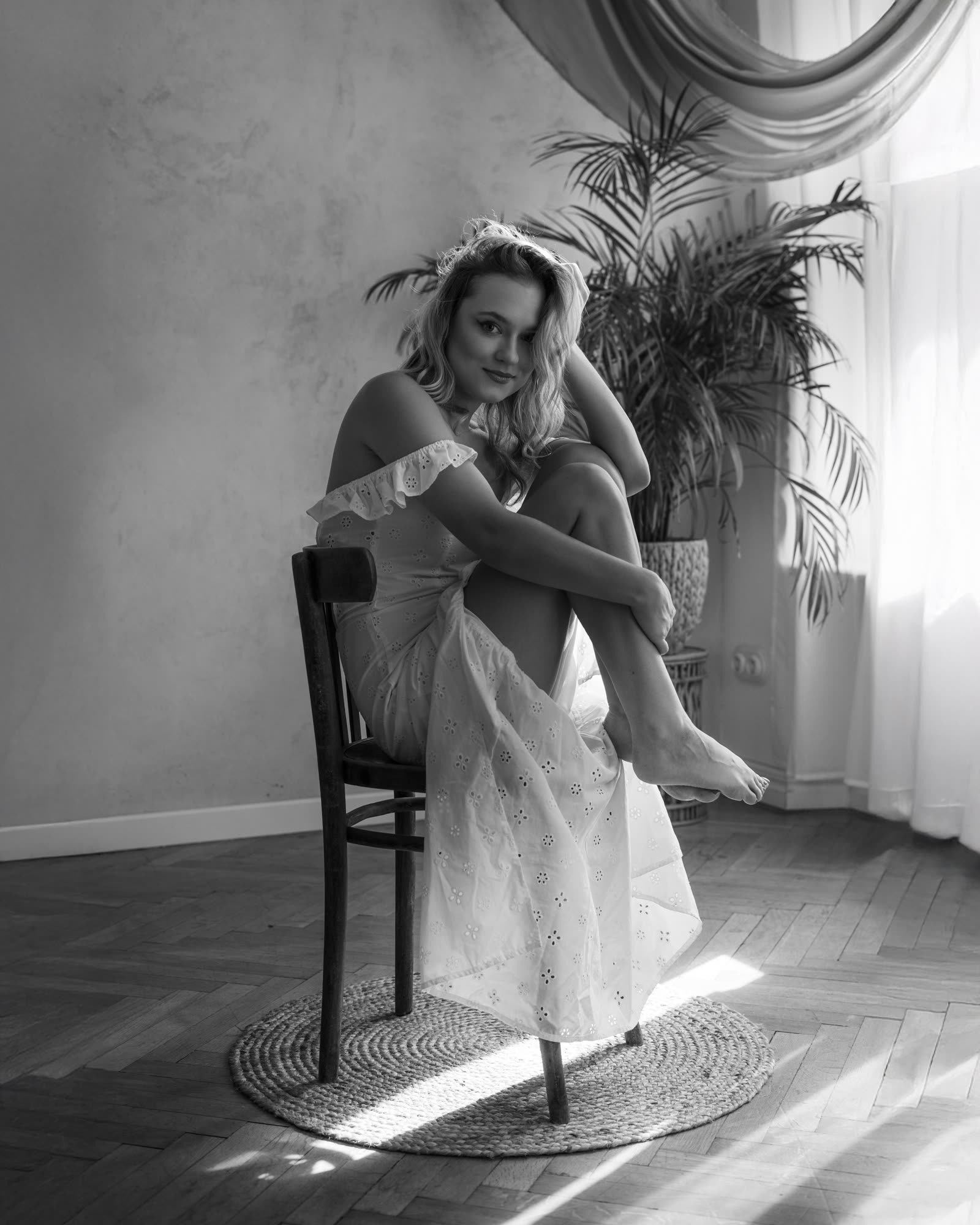 Black and white vintage-style portrait — woman in a linen dress on a wooden chair, atelier interior